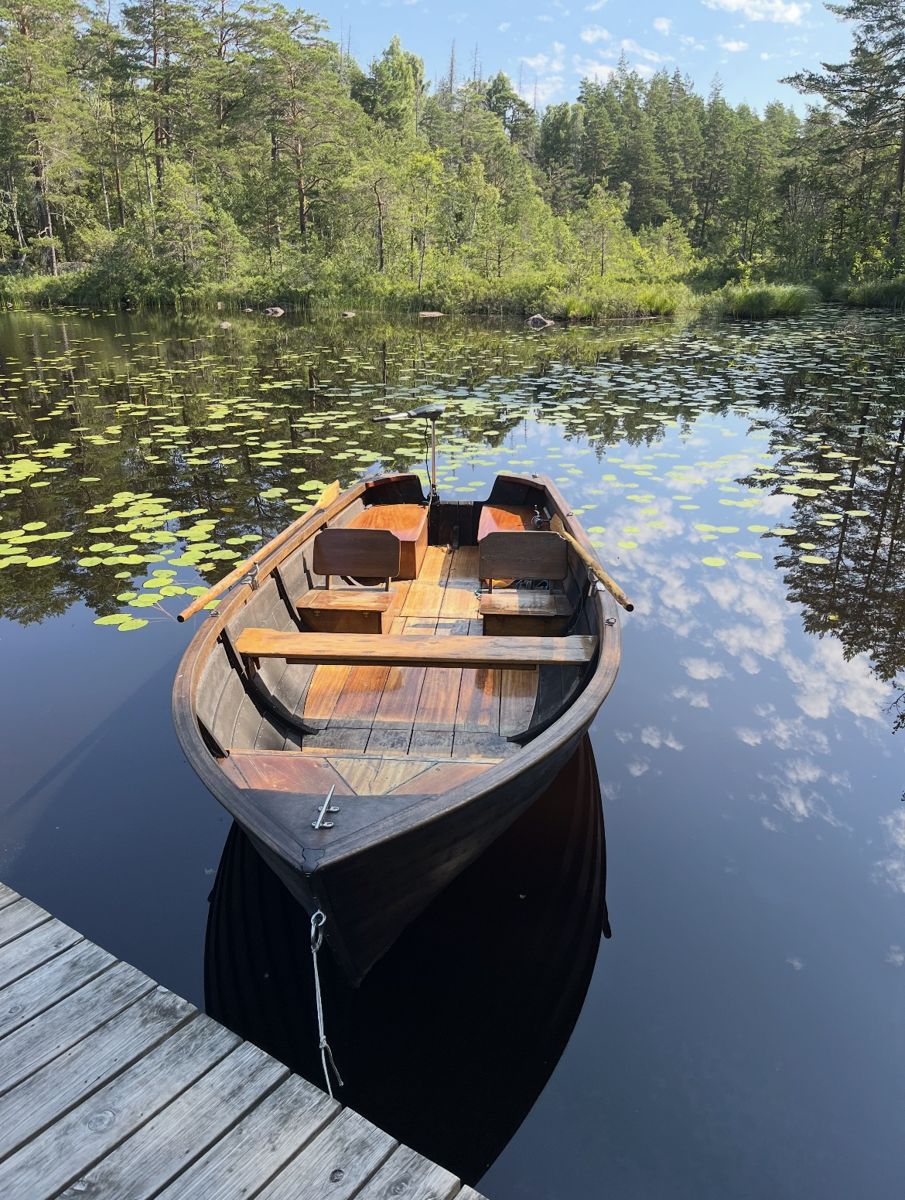 En träeka förtöjd vid en brygga i en stilla skogssjö med näckrosor